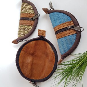 May include: Three small, zippered pouches. One is a half-circle shape with brown and tan tweed fabric, another is a half-circle shape with blue denim, and the third is a brown leather circle. All have brown trim.