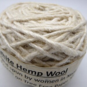 Peut inclure: Gros plan sur une pelote de laine de chanvre blanche. Le fil est &eacute;troitement enroul&eacute; et a un aspect l&eacute;g&egrave;rement textur&eacute;. L'&eacute;tiquette indique "White Hemp Wool". Ce fil est fil&eacute; par des femmes au N&eacute;pal.