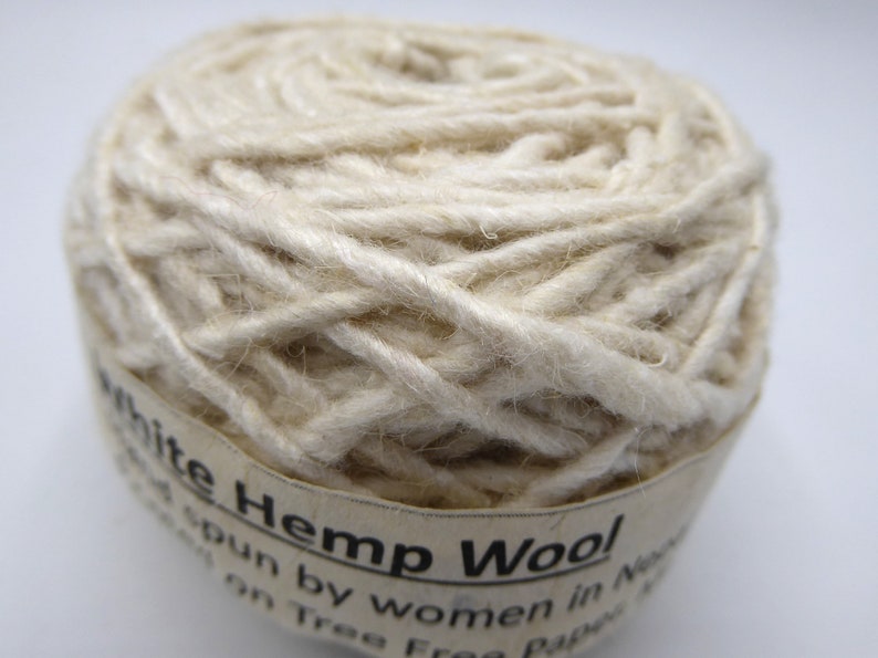Peut inclure: Gros plan sur une pelote de laine de chanvre blanche. Le fil est &eacute;troitement enroul&eacute; et a un aspect l&eacute;g&egrave;rement textur&eacute;. L'&eacute;tiquette indique "White Hemp Wool". Ce fil est fil&eacute; par des femmes au N&eacute;pal.