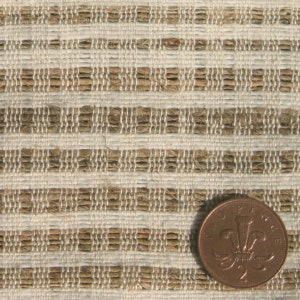 May include: Close-up of a textured fabric with a woven pattern of alternating beige and light brown horizontal stripes. A two pence coin is in the lower right corner for scale. The fabric appears to be made of natural fibers.