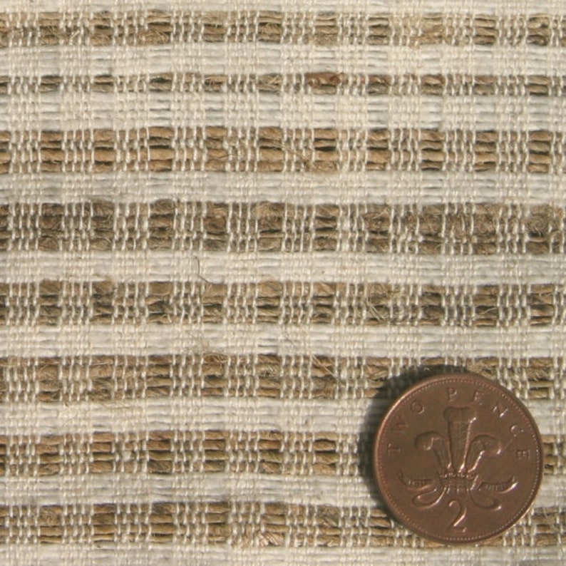 May include: Close-up of a textured fabric with a woven pattern of alternating beige and light brown horizontal stripes. A two pence coin is in the lower right corner for scale. The fabric appears to be made of natural fibers.