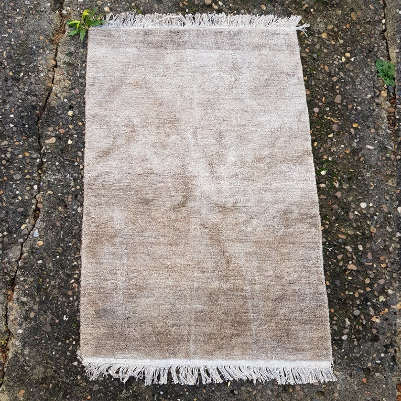 Op de afbeelding: Een rechthoekig, beige tapijt met een getextureerd oppervlak en witte franjes langs de korte uiteinden. Het tapijt heeft een neutraal kleurenpalet, waardoor het geschikt is voor diverse interieurstijlen. De afmetingen van het tapijt zijn niet zichtbaar.