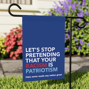 May include: A blue garden flag with white text that reads "Let's stop pretending that your racism is patriotism. Hate never made any nation great."