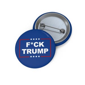 May include: A blue button with a white border and red stars. The text "F*CK TRUMP" is printed in white letters inside the border.