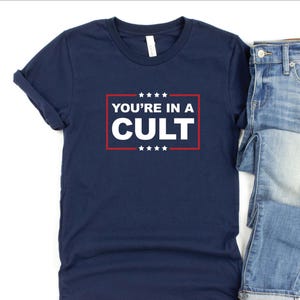 May include: A navy blue t-shirt with a white graphic that says "YOU'RE IN A CULT" in a red and white box with stars.