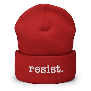 May include: Red knit beanie with a white embroidered word "resist."