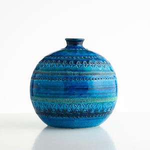 Può includere: Un vaso sferico in ceramica con una smaltatura blu profondo e turchese. La superficie è decorata con fasce orizzontali di motivi geometrici in rilievo, tra cui file di piccoli cerchi, triangoli e disegni a tratteggio incrociato sul corpo.