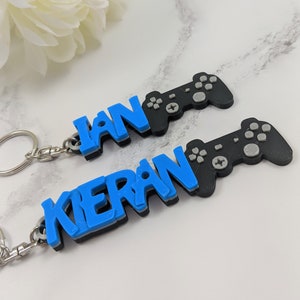 May include: Two blue and black personalized keychains with the names "Ian" and "Kieran" and a black video game controller charm.