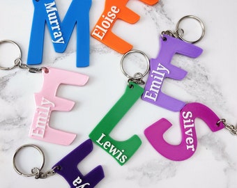 May include: A collection of colorful, personalized keychains featuring the letters 'M', 'E', 'E', 'L', 'S', and 'F' with names printed on each. The keychains are made of plastic and have a silver metal ring.