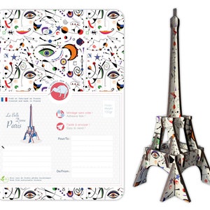 May include: A white cardboard Eiffel Tower model with a colorful abstract pattern. The model is 100 grams and is easy to assemble. The packaging includes a postcard with the same pattern and the text "La Belle Dame Paris".