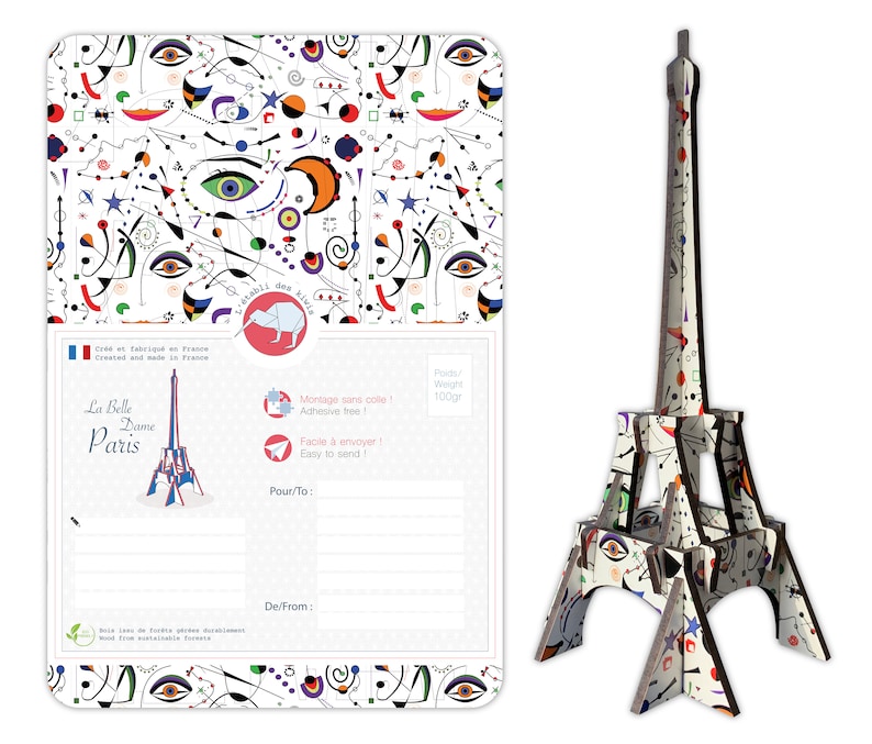 May include: A white cardboard Eiffel Tower model with a colorful abstract pattern. The model is 100 grams and is easy to assemble. The packaging includes a postcard with the same pattern and the text "La Belle Dame Paris".