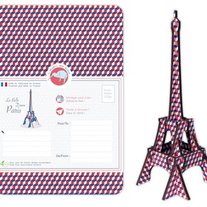 May include: A postcard featuring a red, white, and blue geometric pattern with a small illustration of the Eiffel Tower. The postcard has a space for a message and the text "La Belle Dame Paris" on the front. The postcard is made from wood from sustainable forests.
