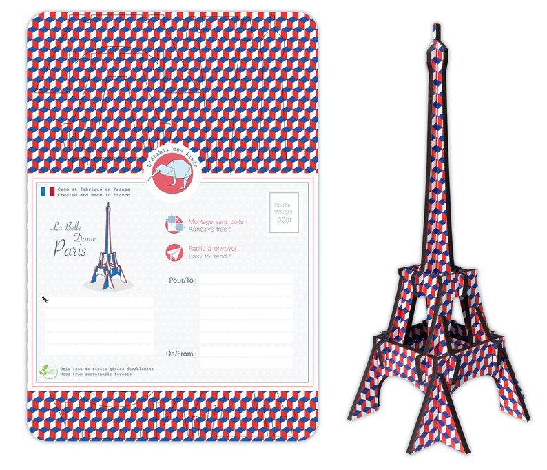 May include: A postcard featuring a red, white, and blue geometric pattern with a small illustration of the Eiffel Tower. The postcard has a space for a message and the text "La Belle Dame Paris" on the front. The postcard is made from wood from sustainable forests.