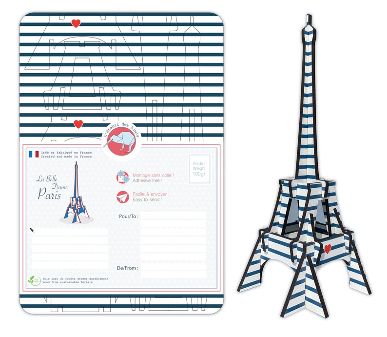 May include: A blue and white striped Eiffel Tower model postcard kit. The postcard features a red heart, the text "La Belle Dame Paris", and a kiwi bird logo. The kit is made of wood from sustainable forests and is easy to assemble.