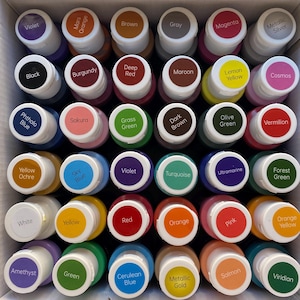 May include: A set of 24 paint bottles in a variety of colours, including violet, orange, brown, grey, magenta, silver, black, burgundy, red, maroon, yellow, cosmos, blue, green, turquoise, ultramarine, white, forest green, cerulean blue, gold, salmon, and viridian.