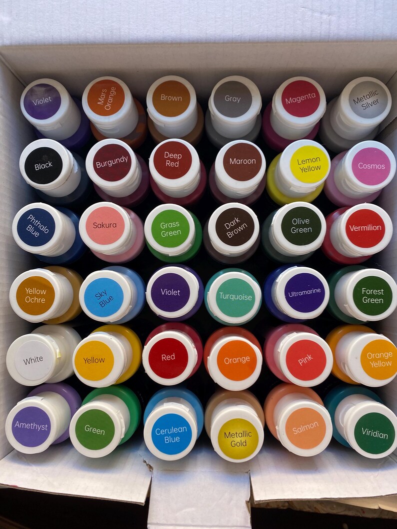 May include: A set of 24 paint bottles in a variety of colours, including violet, orange, brown, grey, magenta, silver, black, burgundy, red, maroon, yellow, cosmos, blue, green, turquoise, ultramarine, white, forest green, cerulean blue, gold, salmon, and viridian.