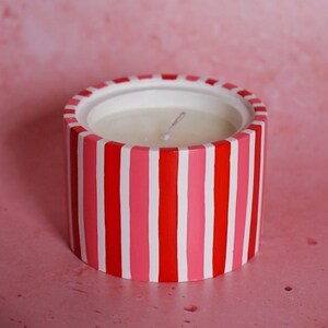 May include: A white candle in a cylindrical container with alternating red and pink vertical stripes.