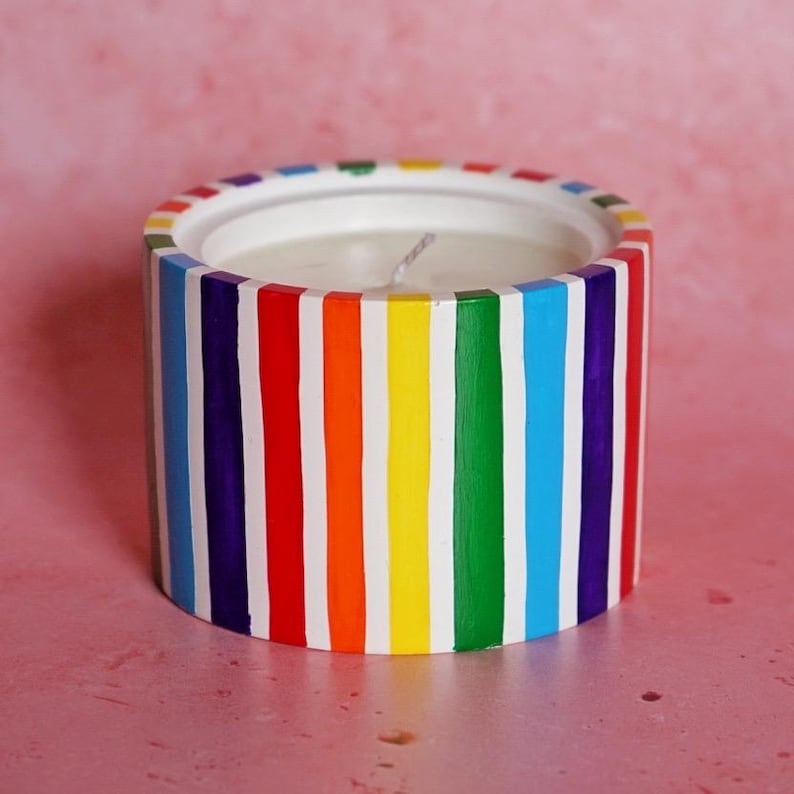 May include: A white candle in a rainbow striped container. The candle is made from soy wax and is hand-poured.