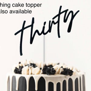 May include: Black cake topper with the word "thirty" written in a script font. The cake topper is on a black and white cake.
