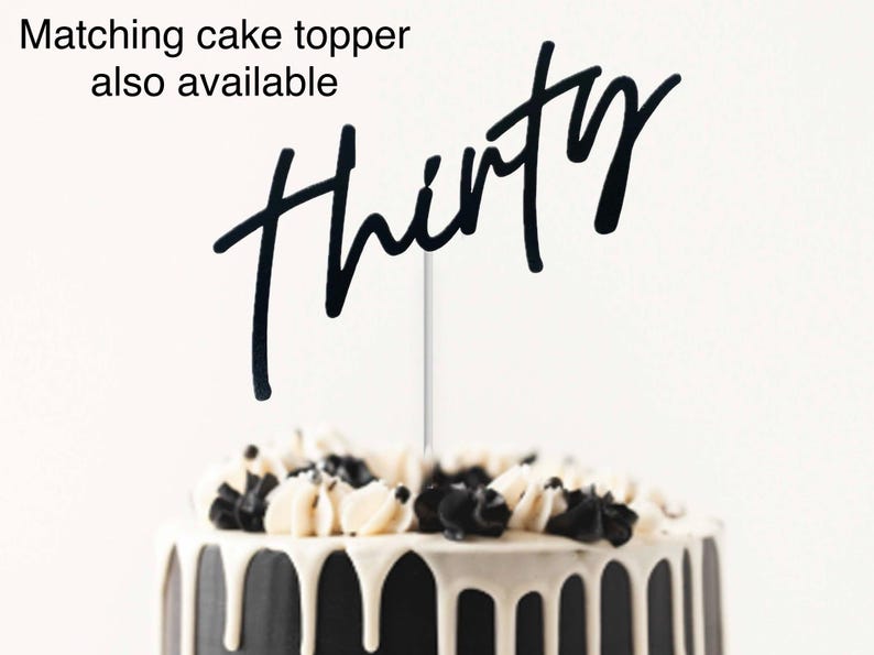 May include: Black cake topper with the word "thirty" written in a script font. The cake topper is on a black and white cake.