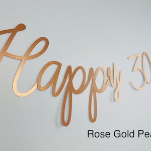 Pode incluir: Uma faixa de p&eacute;rola de ouro rosa com as palavras "Happy 30th" em fonte cursiva. A faixa &eacute; amarrada em uma corda fina e est&aacute; contra um fundo branco. O texto "Rose Gold Pearl" est&aacute; na parte inferior.