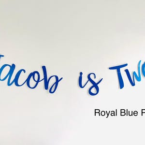 May include: Blue and white cursive lettering that reads "Jacob is Two" with the words "Royal Blue Pearl" below.