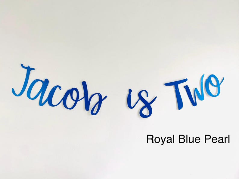 May include: Blue and white cursive lettering that reads "Jacob is Two" with the words "Royal Blue Pearl" below.