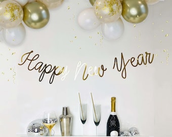 Puede incluir: Una escena festiva de Nochevieja con globos dorados y blancos, una pancarta de "Feliz Año Nuevo", champán, copas y una coctelera. Confeti y bolas de discoteca contribuyen al ambiente festivo.