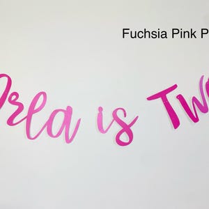 May include: Pink and fuchsia banner with the text "Orla is Two" in a cursive font.