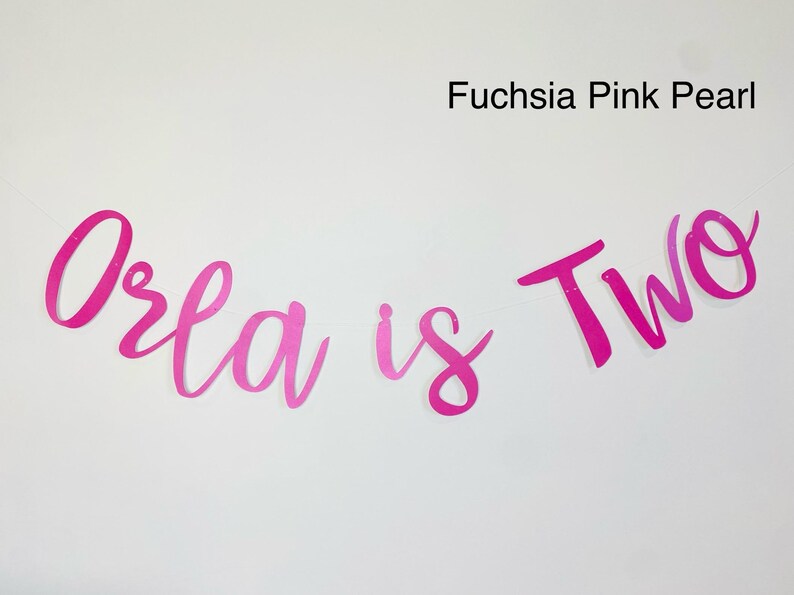 May include: Pink and fuchsia banner with the text "Orla is Two" in a cursive font.