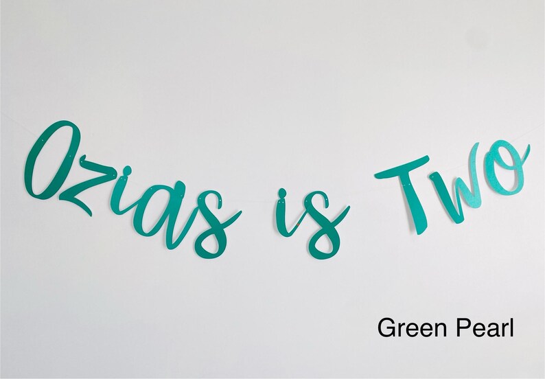 May include: A teal green banner with the text "Ozias is Two" in a cursive font. The banner is on a white background. Green Pearl.
