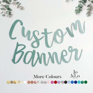 May include: A sage green custom banner featuring cursive lettering. The text reads Custom Banner. Below the text, the words More Colours appear next to the Jo & Lo Designs logo, followed by a horizontal row of twenty-four small circular colour swatches.