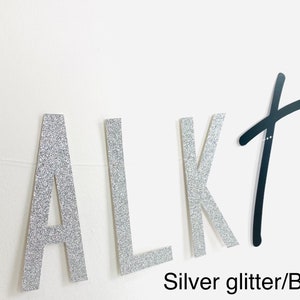 May include: Silver glitter letters spelling "TALK" and black script letters spelling "THIRTY" on a white wall.