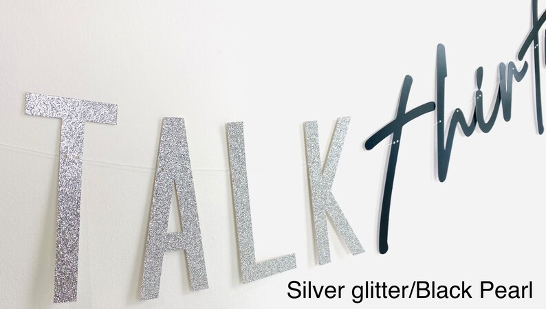 May include: Silver glitter letters spelling "TALK" and black script letters spelling "THIRTY" on a white wall.