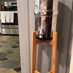 May include: A silver water filter pitcher with a wooden stand. The pitcher has a stainless steel finish and a clear plastic lid. The stand is made of natural wood and has a simple design.