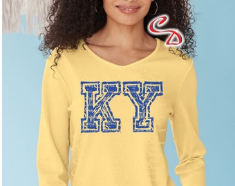 May include: A yellow long-sleeved shirt with a blue and white "KY" graphic. The letters are in a vintage collegiate style with a distressed look. The shirt is a great option for fans of the University of Kentucky.