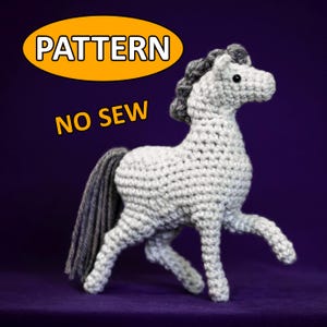 Könnte beinhalten: Ein gehäkeltes graues Pferd mit einer grauen Mähne und einem grauen Schweif. Das Pferd steht auf einer violetten Oberfläche. Der Text "PATTERN NO SEW" ist im Bild sichtbar.