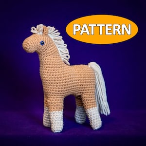 May include: A crocheted brown horse with a white mane and tail. The horse has blue eyes and white hooves. The horse is standing on a purple background. The word "PATTERN" is written in white letters on an orange oval.