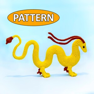 Puede incluir: Un dragón amarillo de ganchillo hecho a mano con detalles rojos. El dragón tiene un cuerpo largo y sinuoso, patas pequeñas y una cola larga. El texto "PATTERN" está en un óvalo amarillo encima del dragón.