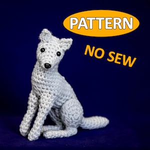 Könnte beinhalten: Ein gehäkelter grauer Wolf, der auf einem blauen Hintergrund sitzt. Der Wolf hat schwarze Augen und eine schwarze Nase. Der Text "PATTERN NO SEW" befindet sich in der oberen rechten Ecke des Bildes.