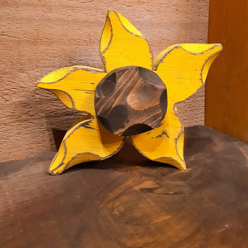 May include: A wooden sunflower with a yellow painted finish and a dark brown center. The sunflower is a decorative piece with a rustic style.