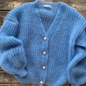 K&ouml;nnte beinhalten: Ein hellblauer Strickcardigan mit Perlmuttkn&ouml;pfen. Der Cardigan hat einen V-Ausschnitt und lange &Auml;rmel.