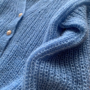 K&ouml;nnte beinhalten: Ein hellblauer, flauschiger Cardigan mit Perlmuttkn&ouml;pfen.