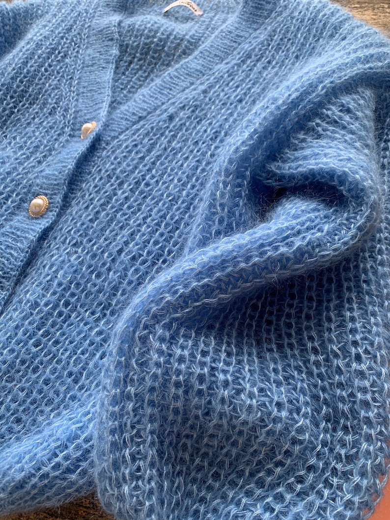 K&ouml;nnte beinhalten: Ein hellblauer, flauschiger Cardigan mit Perlmuttkn&ouml;pfen.