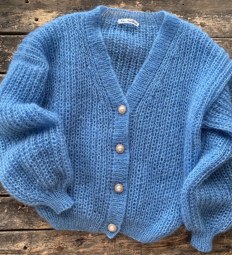 K&ouml;nnte beinhalten: Ein hellblauer Strickcardigan mit Perlmuttkn&ouml;pfen. Der Cardigan hat einen V-Ausschnitt und lange &Auml;rmel.