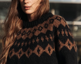 Könnte beinhalten: Ein schwarzer und brauner Pullover mit Muster und Rundhalsausschnitt. Der Pullover ist aus weichem, gestricktem Stoff.