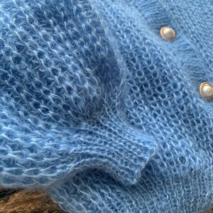 K&ouml;nnte beinhalten: Ein hellblauer, flauschiger Strickcardigan mit Perlenkn&ouml;pfen.