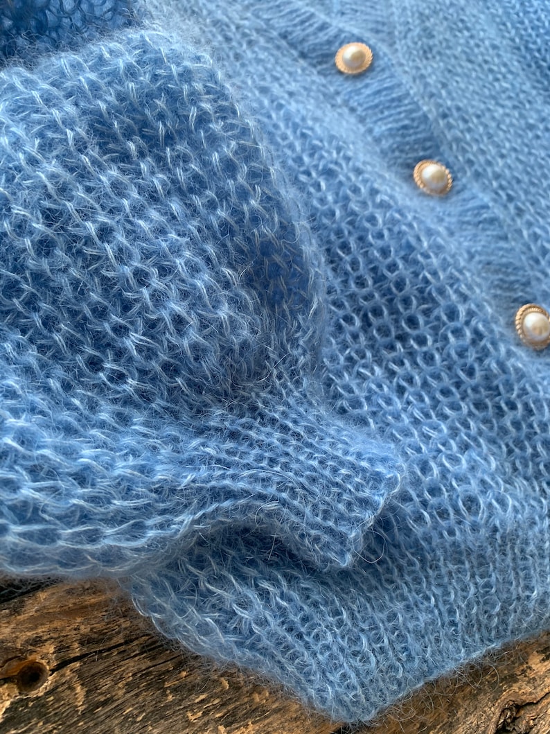 K&ouml;nnte beinhalten: Ein hellblauer, flauschiger Strickcardigan mit Perlenkn&ouml;pfen.