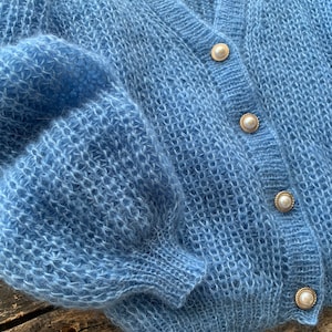 K&ouml;nnte beinhalten: Ein hellblauer, flauschiger Cardigan mit Perlmuttkn&ouml;pfen.