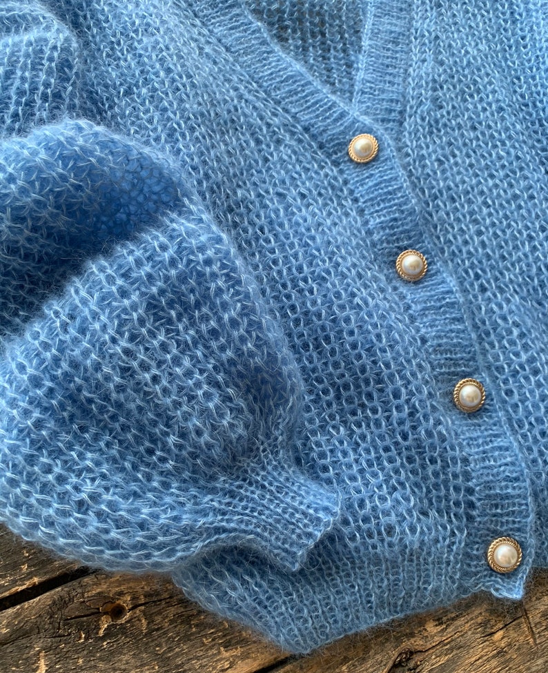 K&ouml;nnte beinhalten: Ein hellblauer, flauschiger Cardigan mit Perlmuttkn&ouml;pfen.